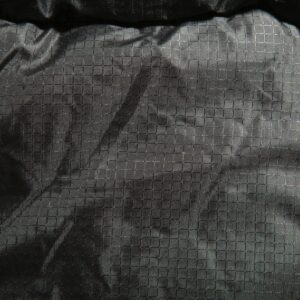 Nahaufnahme eines dunklen, gekräuselten Stoffes mit dezentem Schachbrettmuster und Lichtreflexen - ähnlich der Textur der Maelson Cosy Roll Hundedecke / Autoschondecke in Schwarz oder Beige.